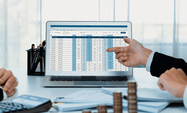 Computer screen displaying a financial spreadsheet with numbers and young professionals pointing to it, illustrating financial planning.