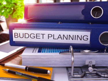 Open binder full of papers with notebooks on top, including one titled 'Budget Planning'.