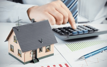 Man using a calculator with a model house and a spreadsheet on the table - How to refinance your home