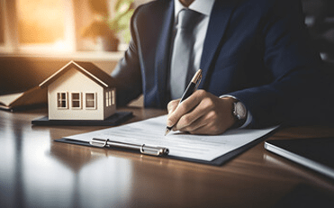 A man in a suit and tie filling out a loan application on a clipboard with a model house next to it, representing "A Beginner’s Guide to Understanding Home Loans"