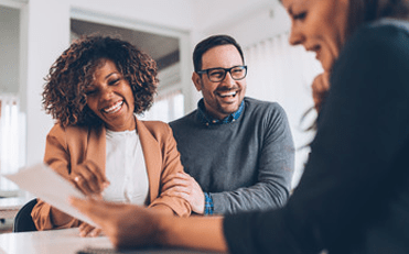 Couple sitting at a table with a financial planner holding a paper, discussing home budget planning.