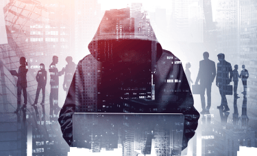 Hacker in a hoodie at a computer with business professionals discussing cybersecurity strategies